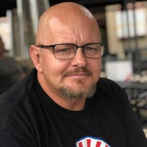 Bald man wearing glasses and a t-shirt.